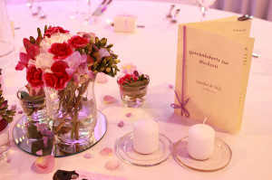 Die Hochzeitsdekoration auf einem Banketttisch mit Blumen, Kerzen und Getränkekarte.