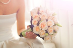 Ein Brautstrauß mit hellen Rosen in der Hand der Braut. 