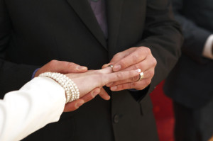 Ein Bräutigam steckt seiner Braut bei der Hochzeit den Ring an den Finger. 
